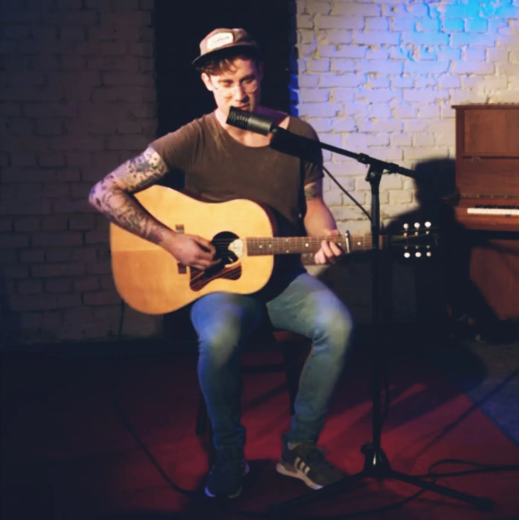Brickwater spielt Akustikgitarre vor einer weißen Backsteinwand